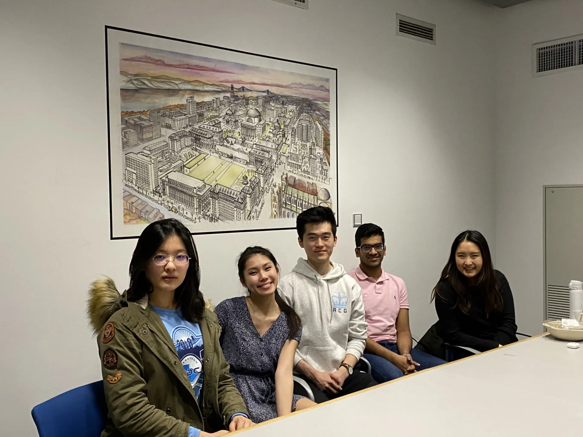 Four ladies and one male are seated at a conference table smiling for a picture.