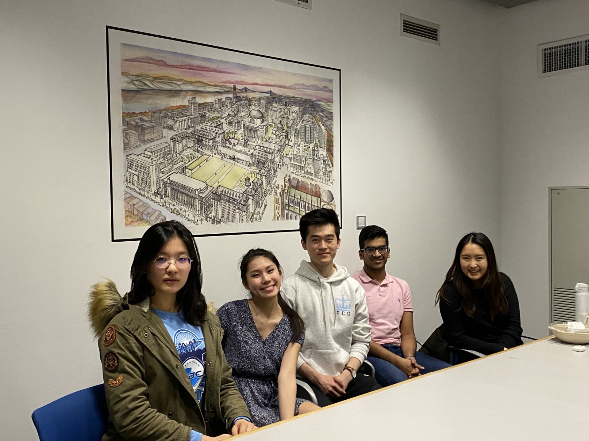 Four ladies and one male are seated at a conference table smiling for a picture.